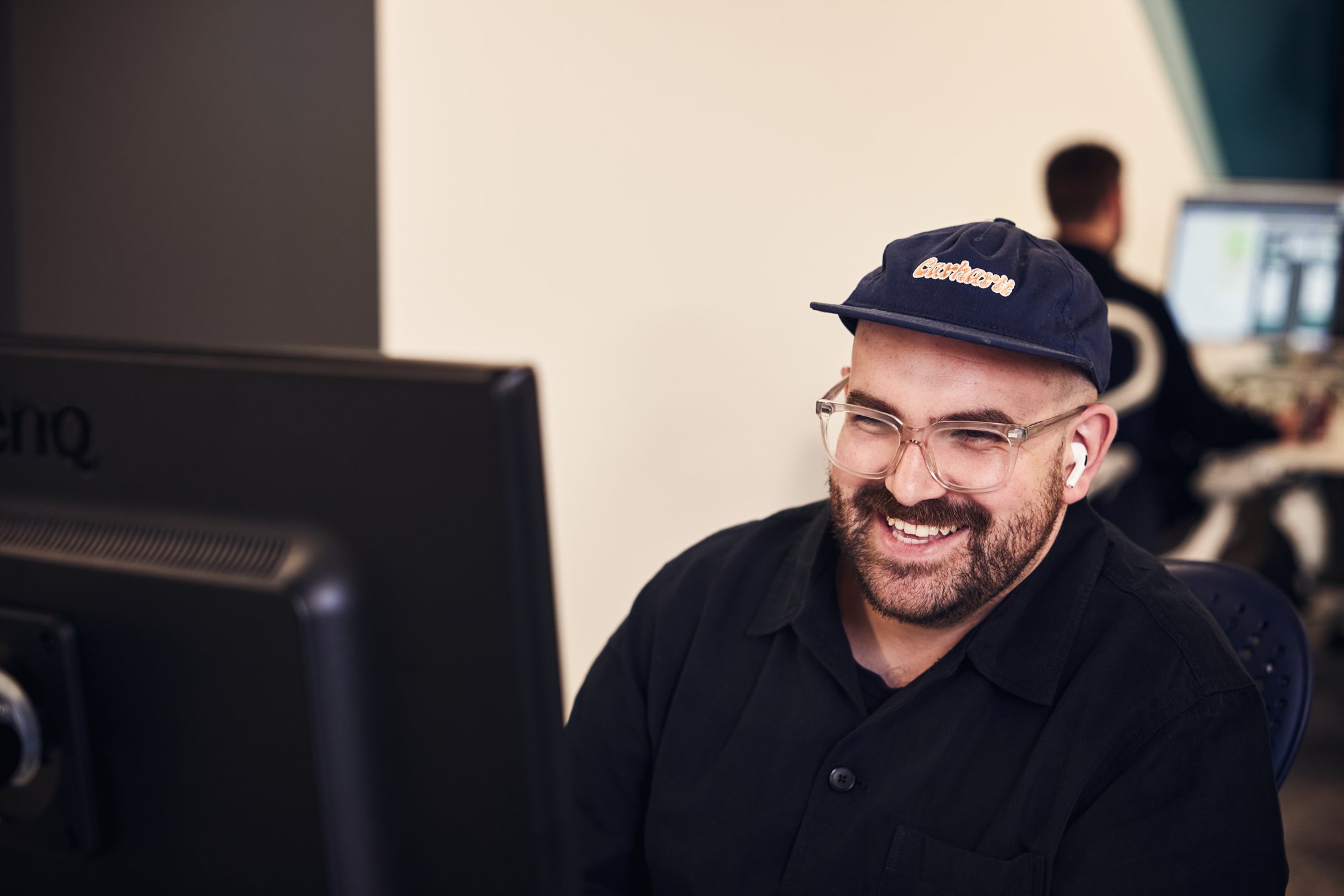 Man wearing a cap, smiling at his computer screen