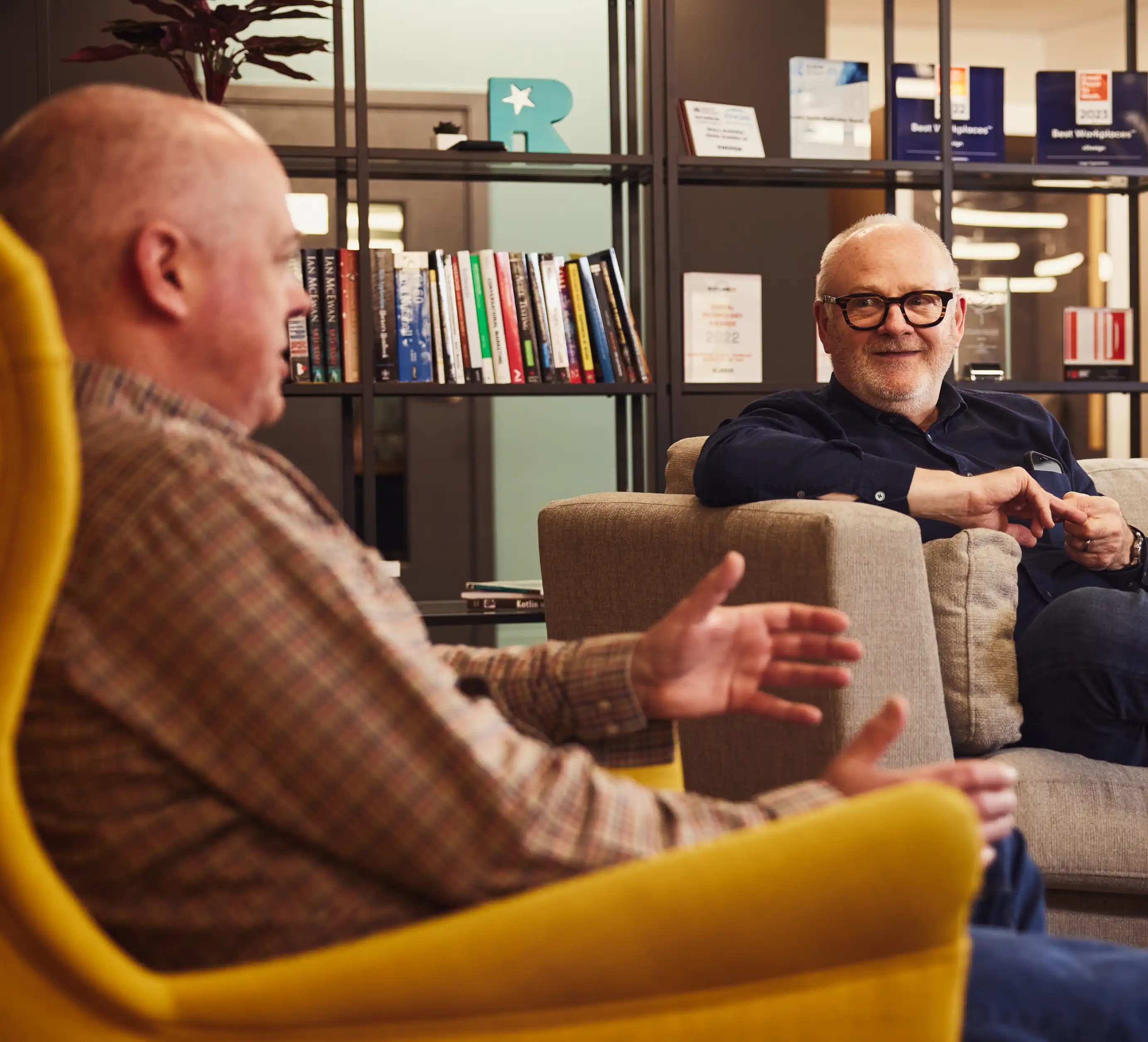 Two colleagues smiling and talking in armchairs.