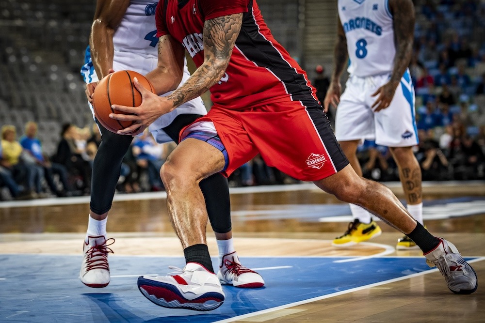 Close-up of basketball players as a player in red tightly holds the ball while being guarded by opponents in white.