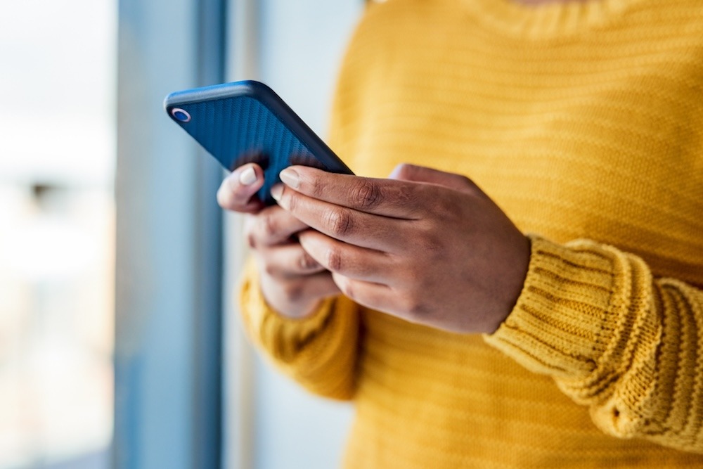 Person in a yellow jumper using a smartphone near a window.