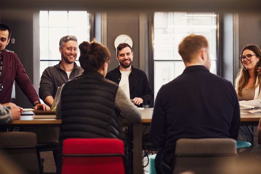 A group of colleagues gathered at a table, chatting and smiling.