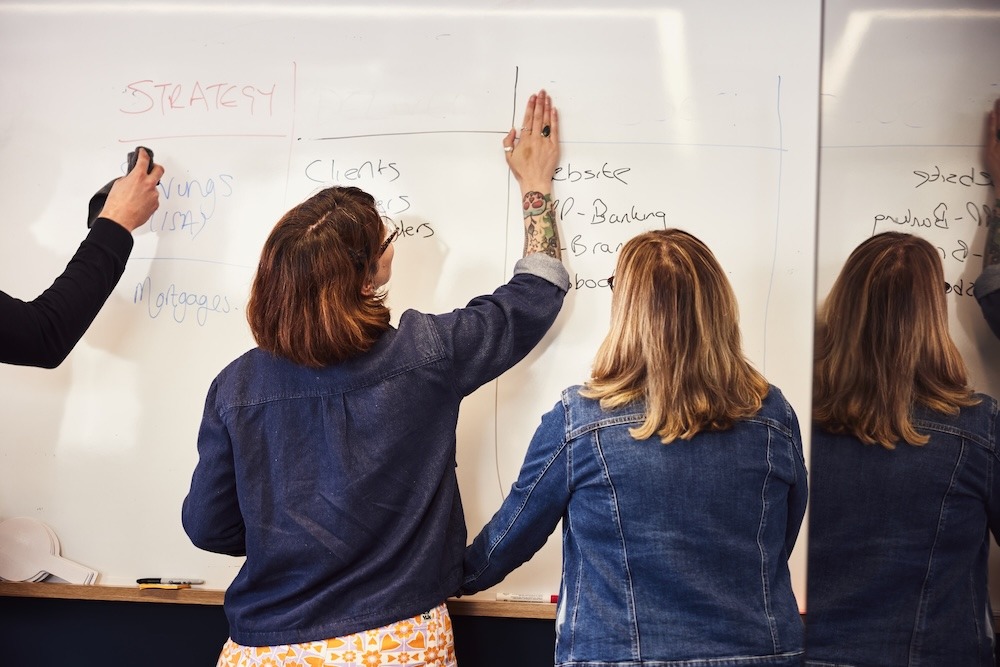 Two colleagues brainstorming and writing down ideas on a whiteboard.