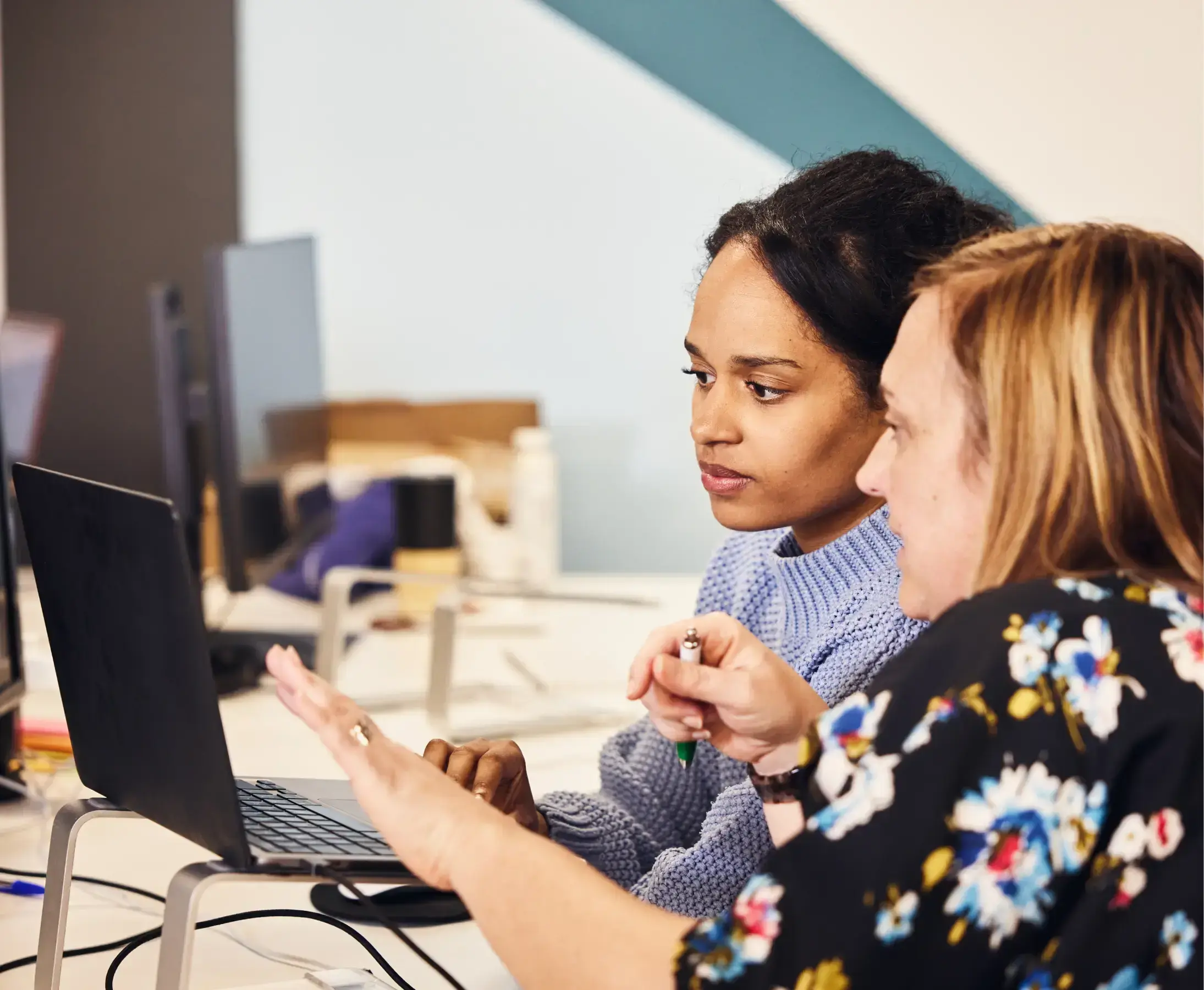 Two colleagues are having a discussion over something they are looking at on a shared laptop screen