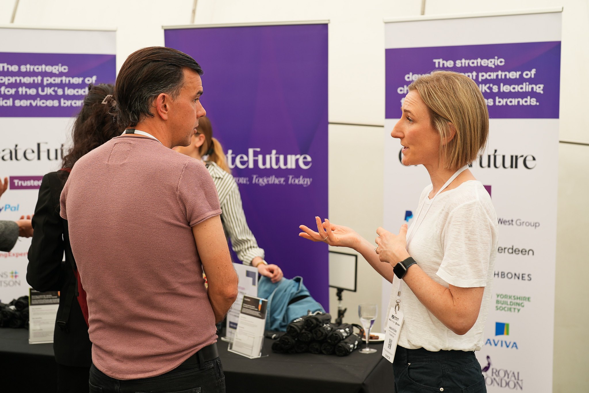 A man and woman wearing lanyards are conversing at a professional event with 