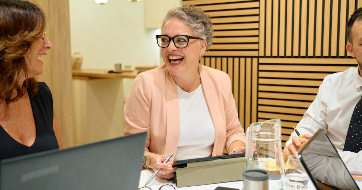 Woman laughing with colleagues during a meeting in a relaxed office setting.