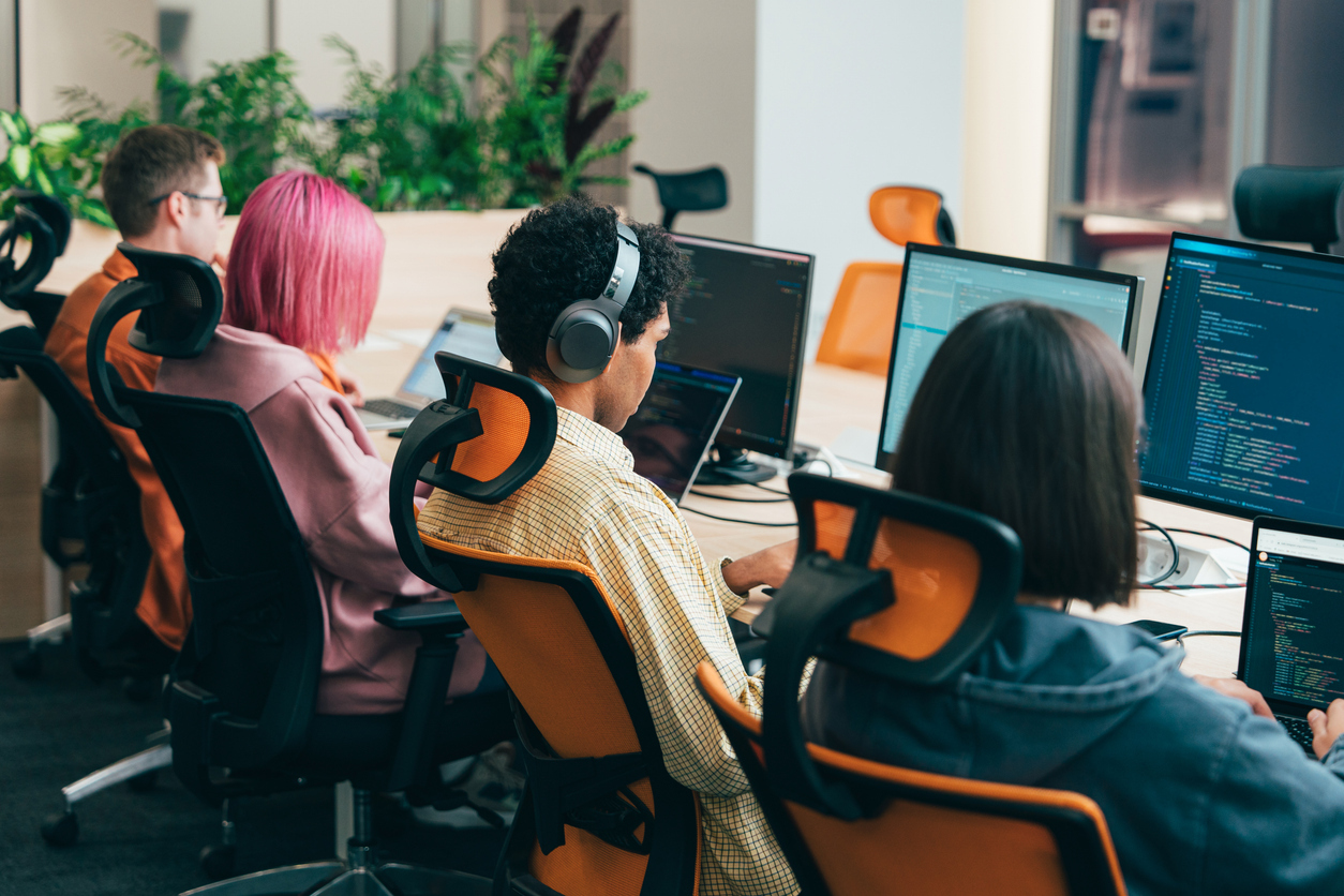 Developers working at desks with multiple monitors displaying code, collaborating in a modern office environment during a coding session